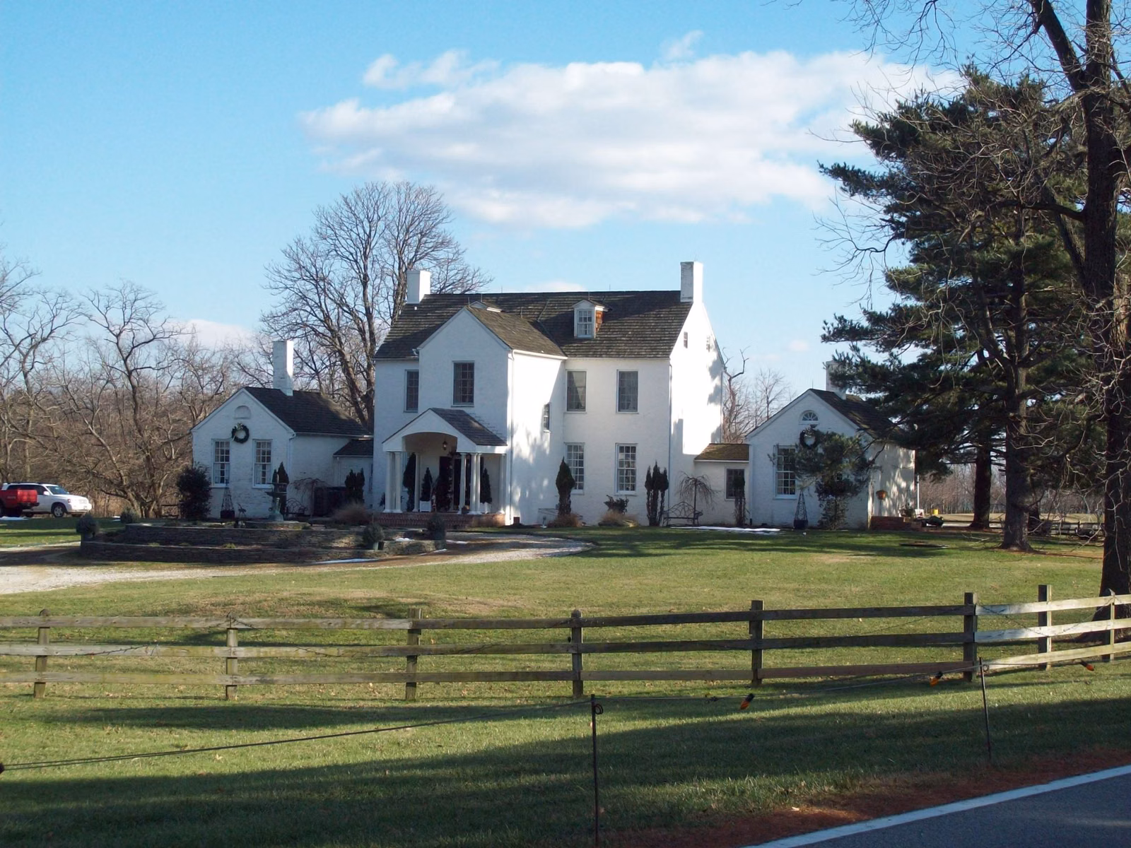 The white Sandy Point Mansion farmhouse behind a split-rail fence in Sandy Point State Park