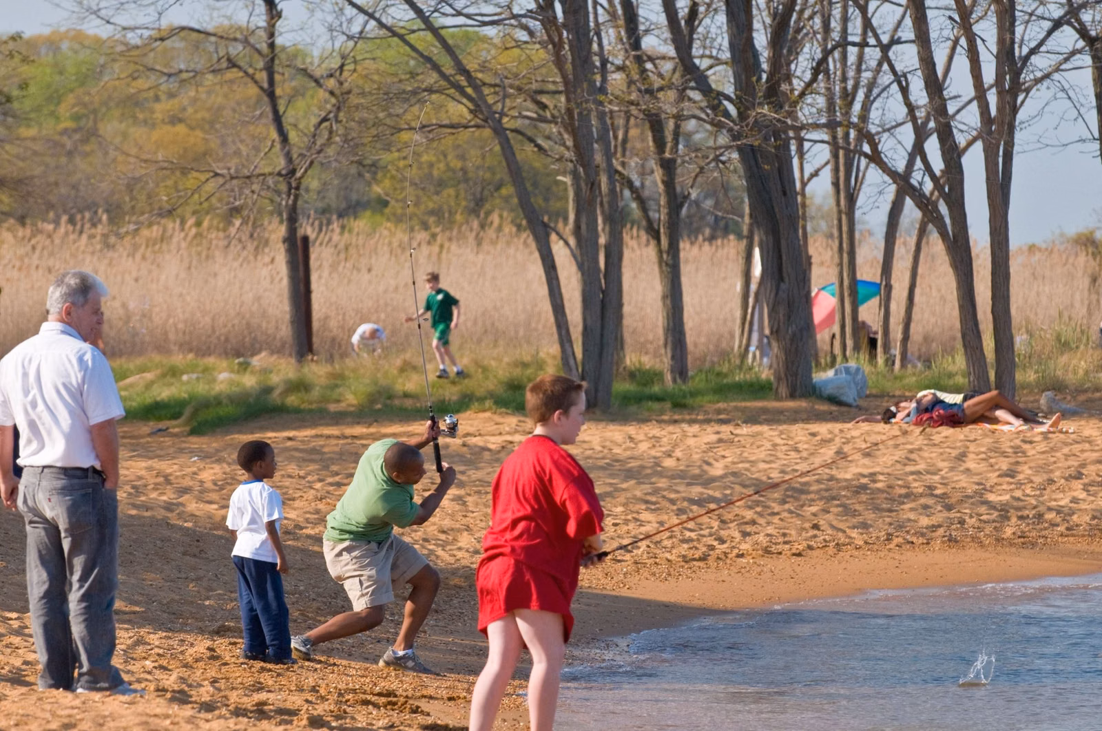 People fishing from the sandy shore at Sandy Point State Park, with marsh grass and trees behind