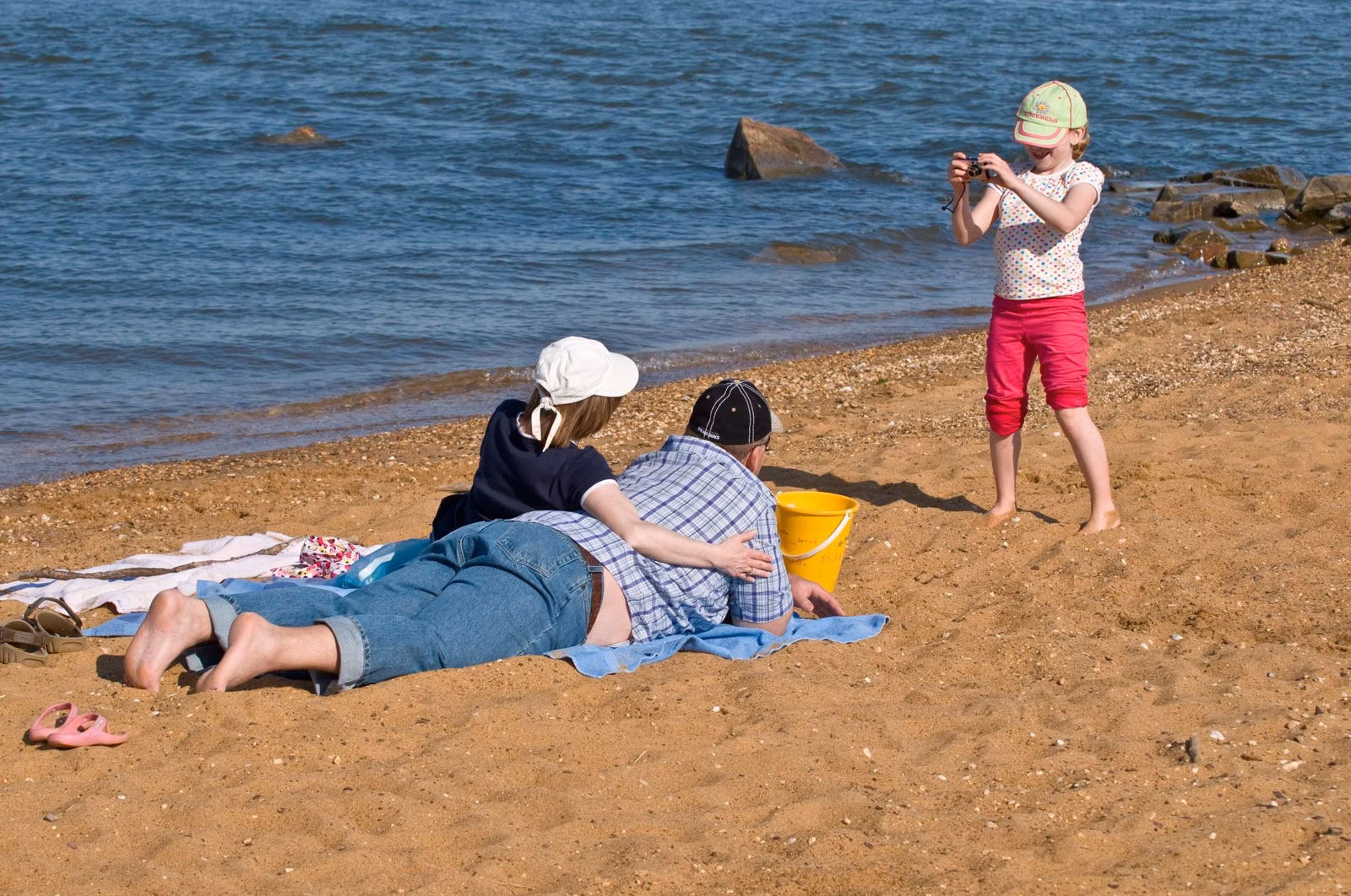 A family relaxing on the sand at Sandy Point State Park beside the Chesapeake Bay, with rocks along the shore